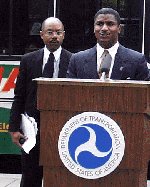 Former U.S. Secretary of Transportation Rodney E. Slater giving some remarks during the electric bus ribbon-cutting ceremony at the U.S. Department of Transportation Headquarters Building in Washington, DC.  Former Federal Transit Administrator Gordon J. Linton is in the background.